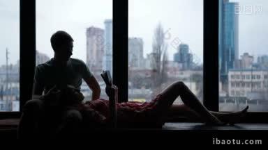 <strong>情侣</strong>在一起休闲和阅读的剪影在城市风景背景美丽的女人在家里的窗台上